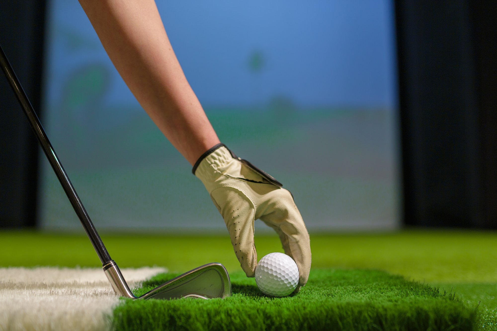 Golfer putting golf ball on golf tee at golf simulator